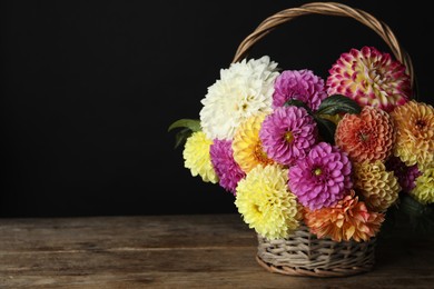 Basket with beautiful dahlia flowers on wooden table against black background. Space for text