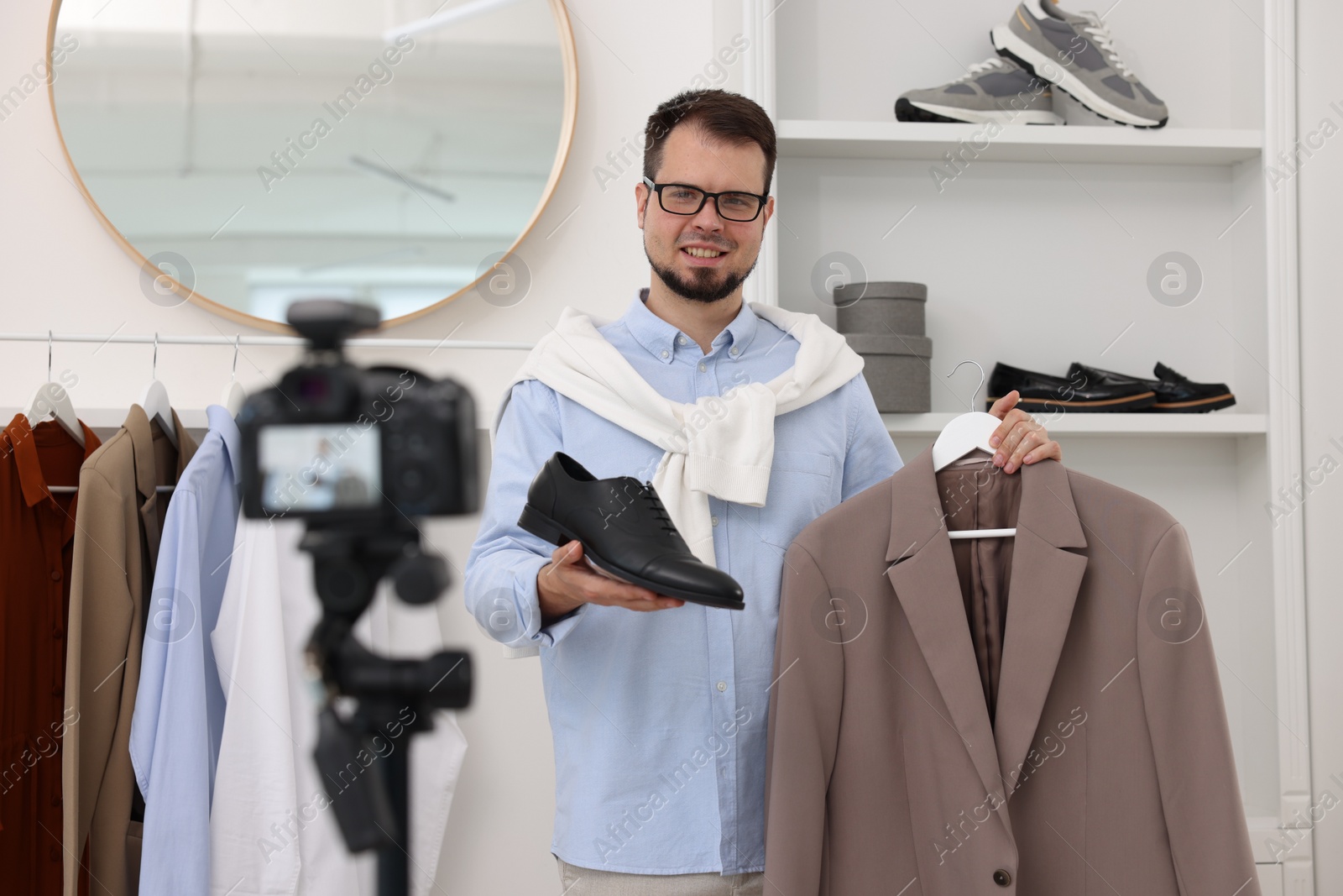 Photo of Smiling fashion blogger showing clothes while recording video at home