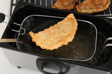 Spatula with delicious fried chebureki over deep fryer, above view