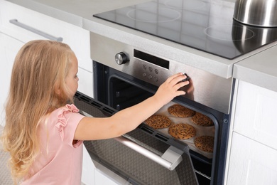 Little girl baking cookies in oven at home