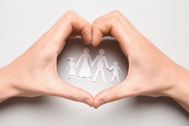 Woman showing heart gesture over paper cutout of family on light background, top view