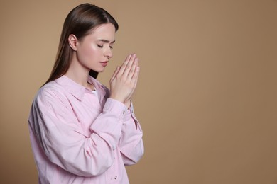 Woman with clasped hands praying on beige background, space for text
