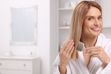 Photo of Beautiful happy woman brushing her hair in room, space for text