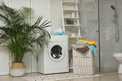 Photo of Wicker basket with laundry and washing machine in bathroom