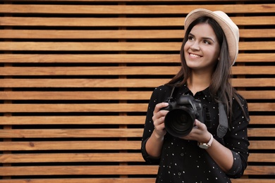 Photo of Young female photographer with professional camera near wooden wall. Space for text