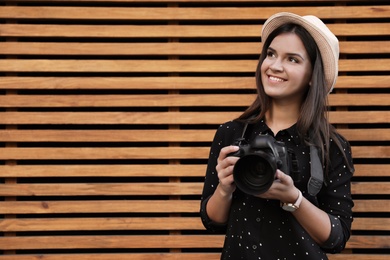 Young female photographer with professional camera near wooden wall. Space for text