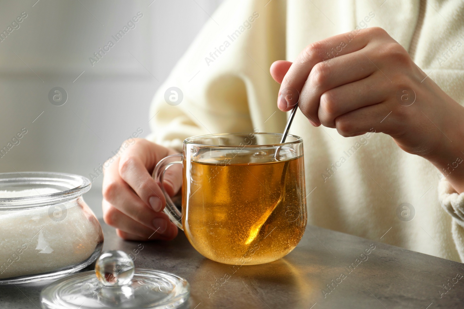 Photo of Woman stirring sugar in tea at grey table, closeup