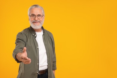 Photo of Senior man in glasses welcoming and offering handshake on yellow background, space for text