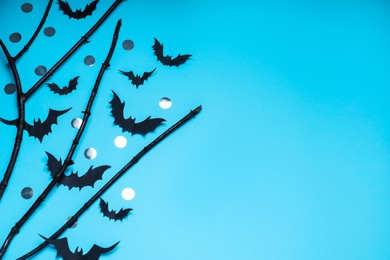 Flat lay composition with black branches and paper bats on light blue background, space for text. Halloween celebration