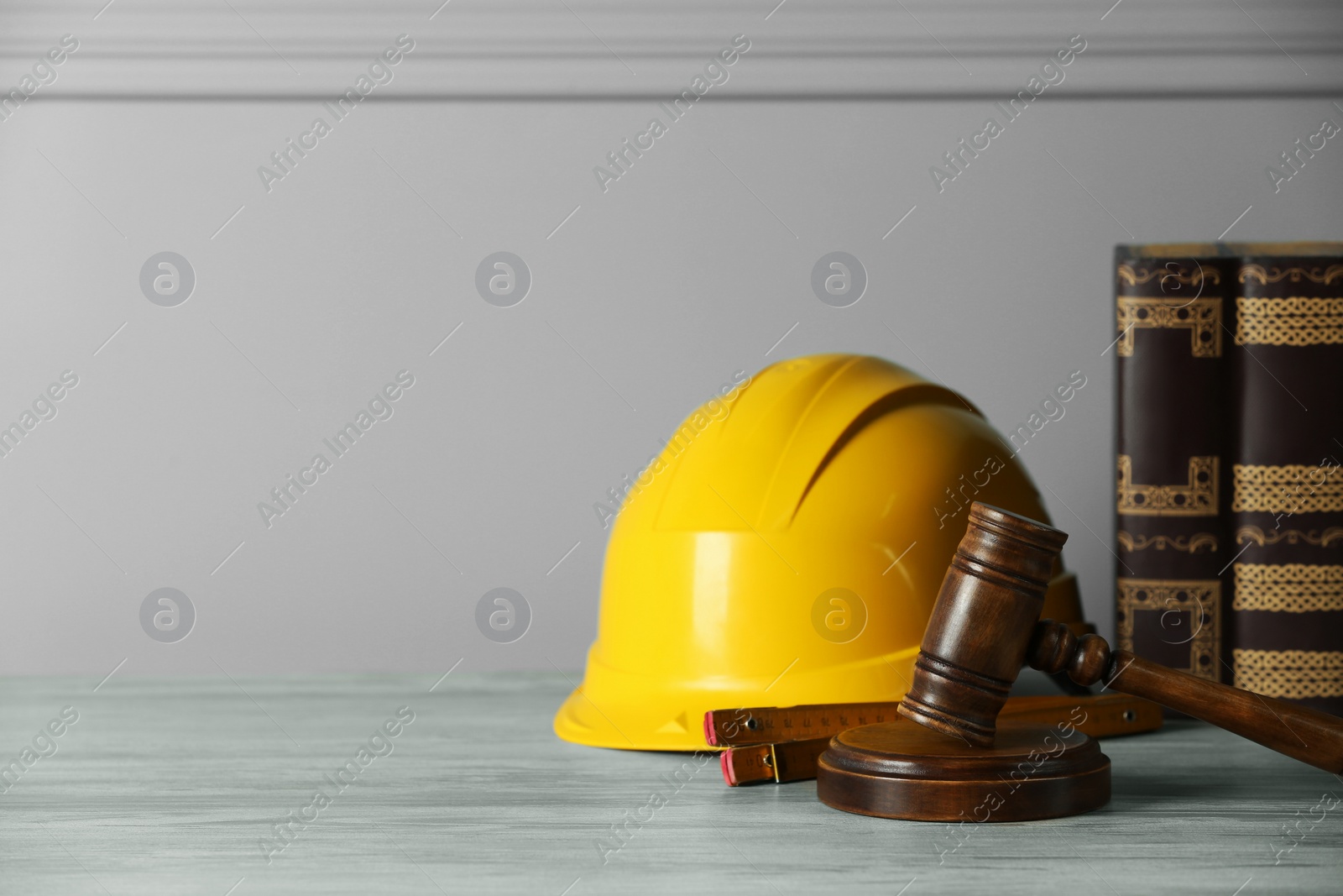 Photo of Construction and land law concepts. Judge gavel, construction helmet, ruler and books on light grey table, space for text