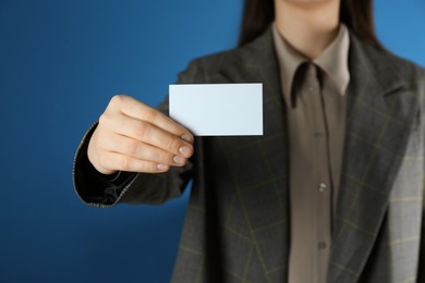 Woman holding white business card on blue background, closeup