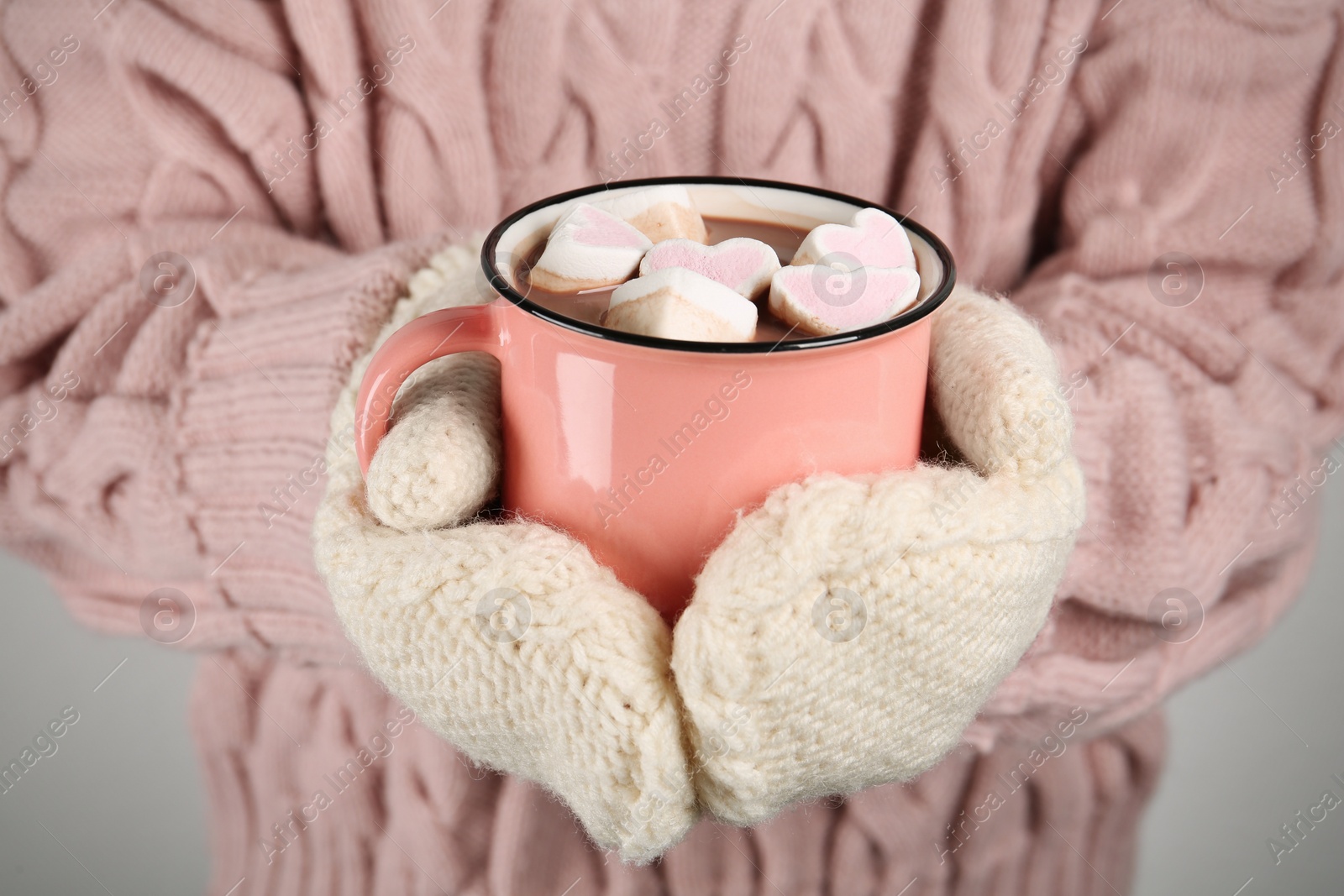 Photo of Woman in knitted mittens holding cup of delicious hot chocolate with marshmallows, closeup