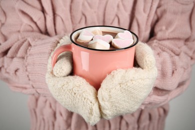 Photo of Woman in knitted mittens holding cup of delicious hot chocolate with marshmallows, closeup