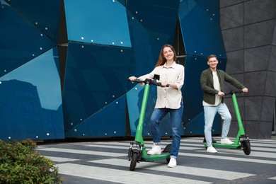 Photo of Happy couple with modern electric kick scooters on city street, space for text