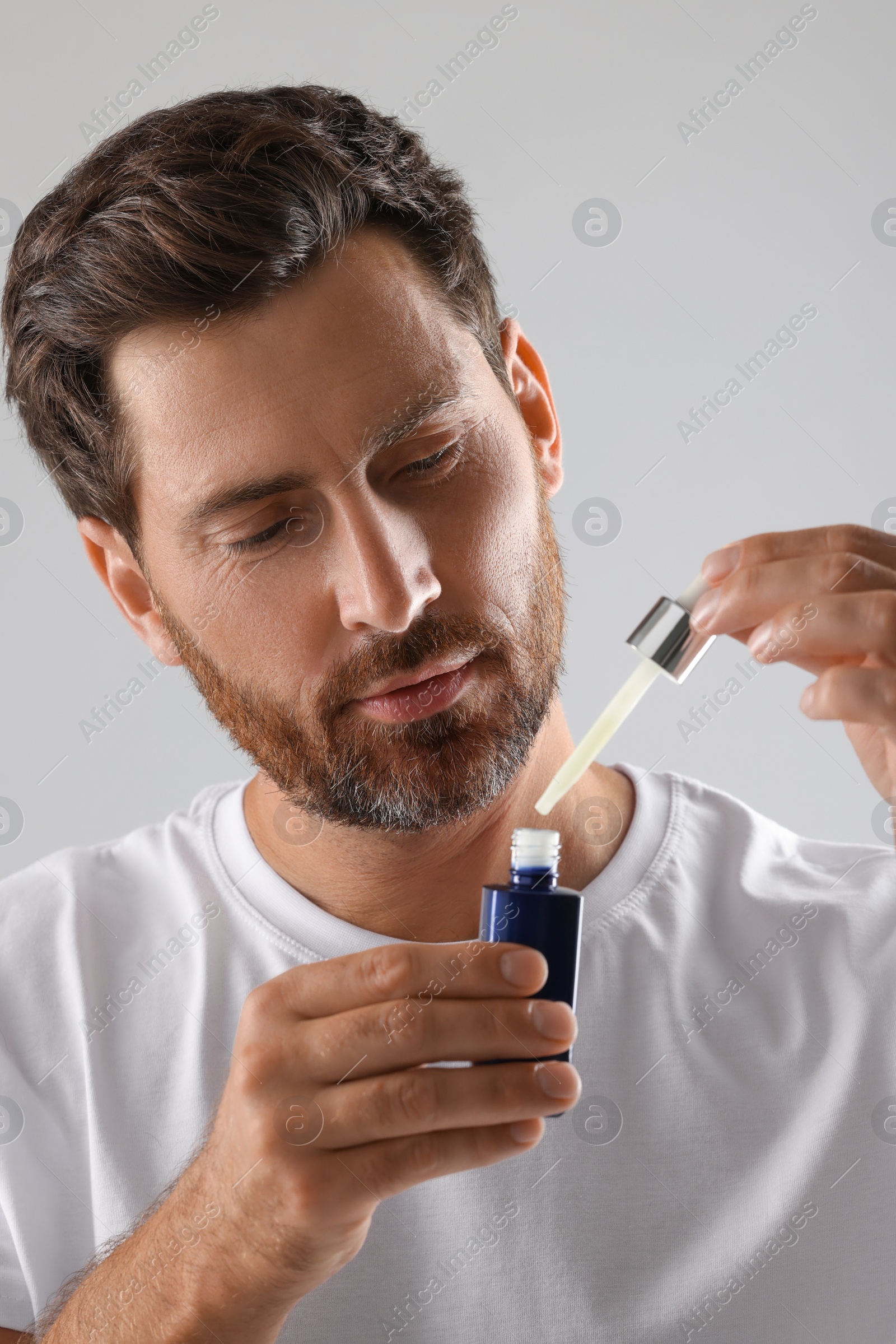 Photo of Handsome man with cosmetic serum on light grey background