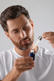 Handsome man with cosmetic serum on light grey background