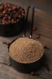 Photo of Aromatic clove powder and dried buds in scoops on wooden table, closeup
