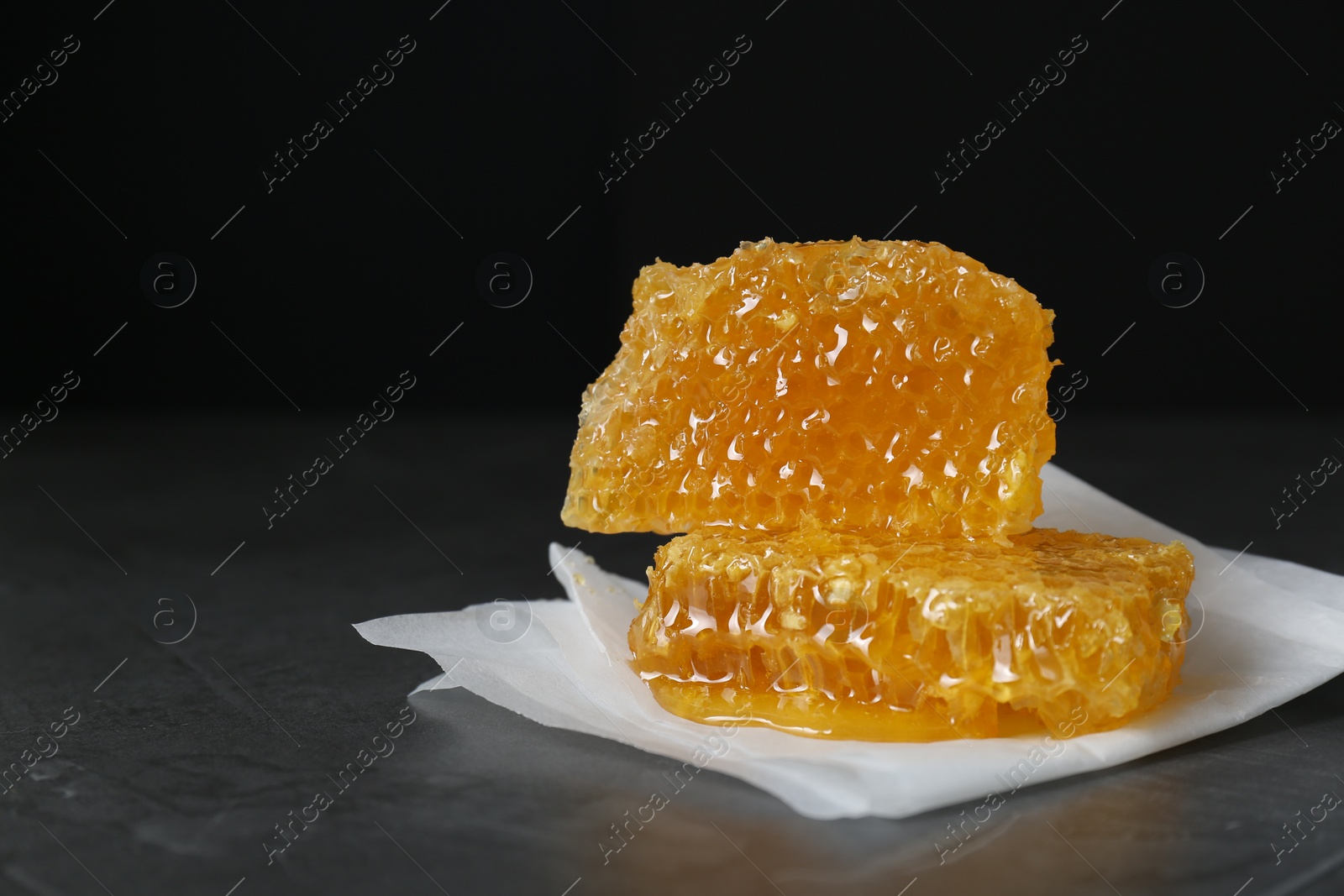 Photo of Natural honeycombs on dark table against black background, space for text