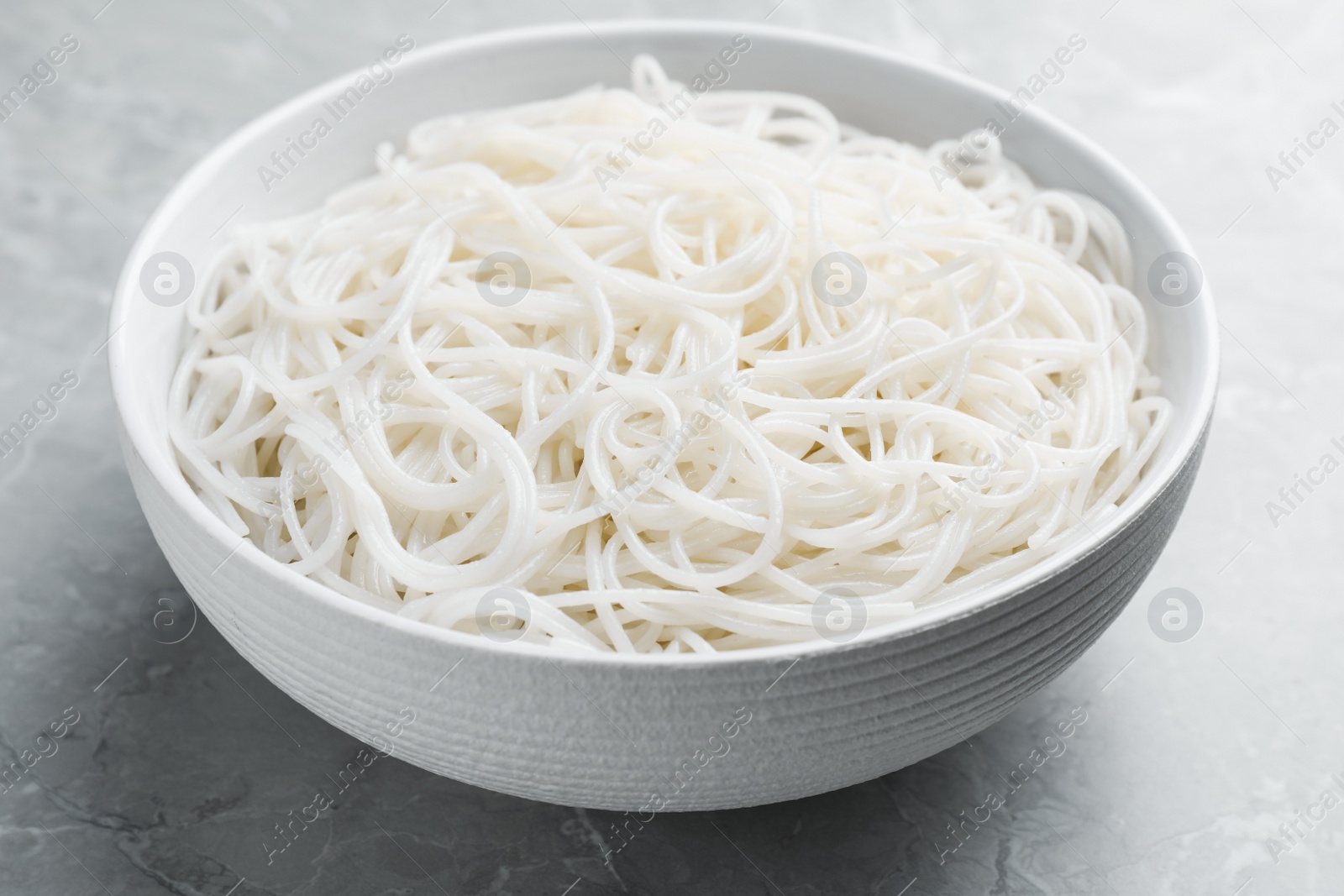 Photo of Bowl with cooked rice noodles on light marble table, closeup