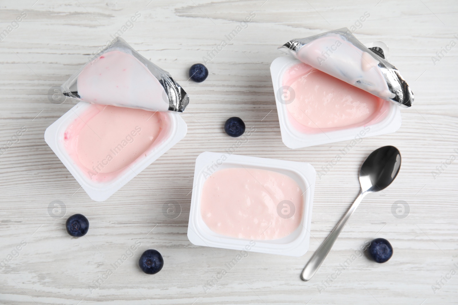 Photo of Plastic cups with tasty yogurts and blueberries on white wooden table, flat lay