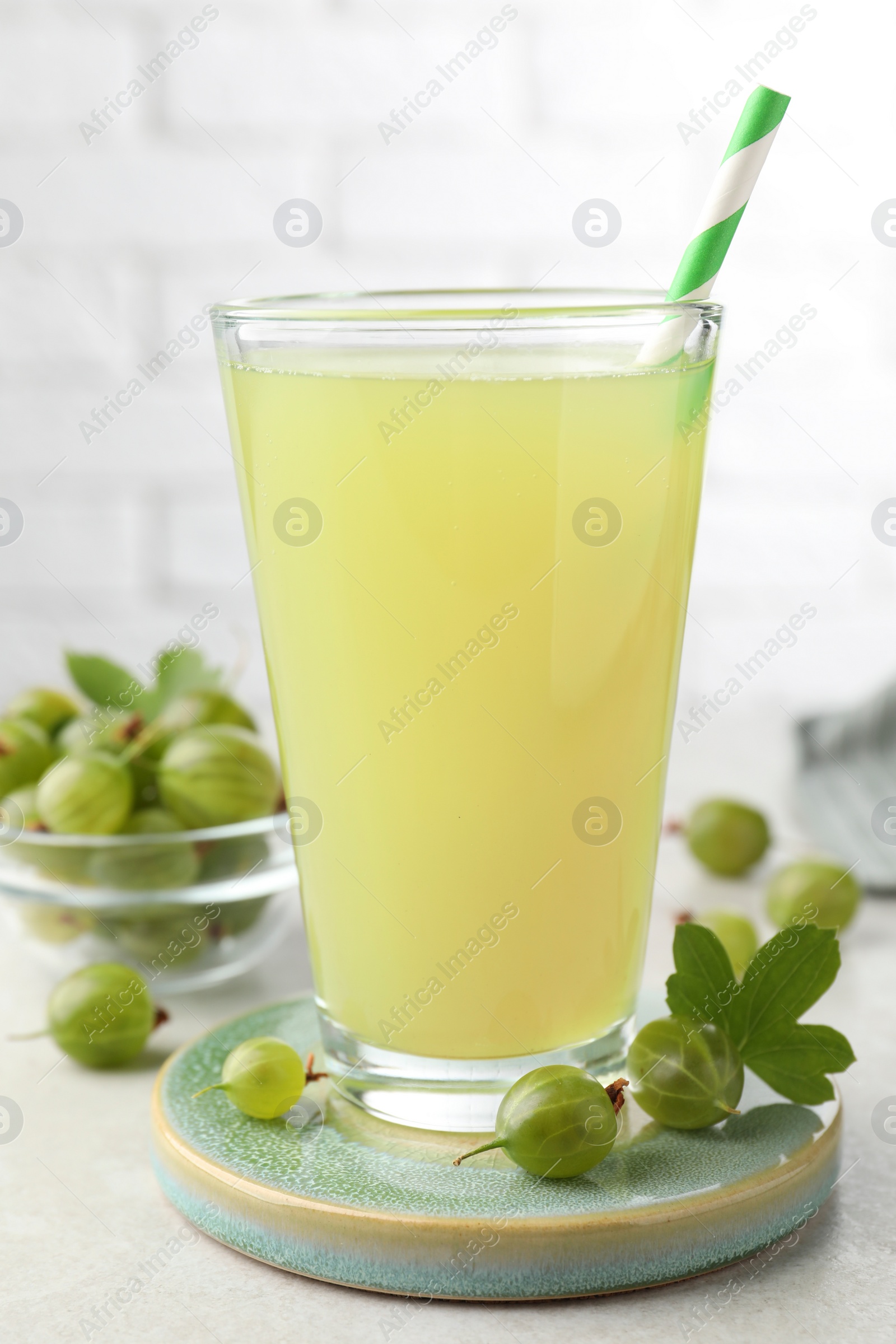 Photo of Tasty gooseberry juice in glass and fresh berries on light table, closeup