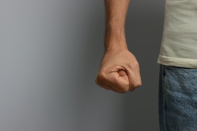Photo of Aggressive man on grey background, closeup view of fist. Space for text