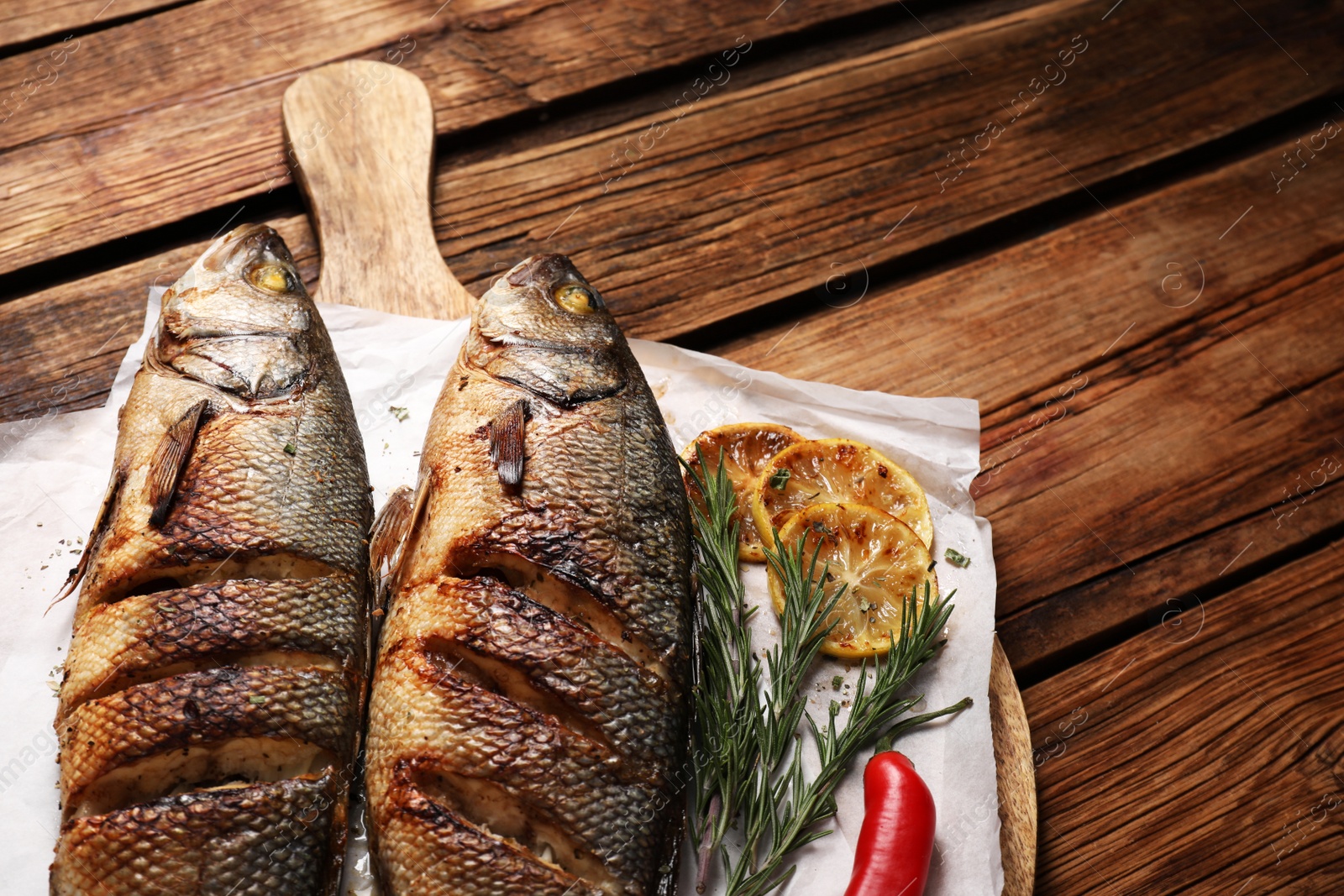 Photo of Delicious baked sea bass fish and ingredients on wooden table, closeup