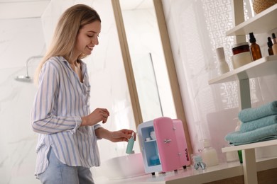 Photo of Woman taking cosmetic product from mini fridge in bathroom