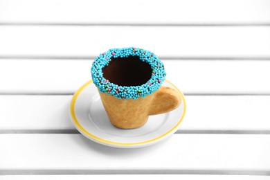 Delicious edible biscuit coffee cup decorated with sprinkles on white wooden surface