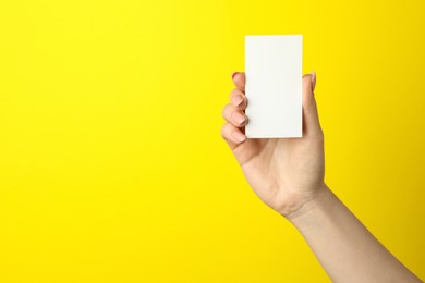 Photo of Woman holding blank business card on yellow background, closeup. Mockup for design