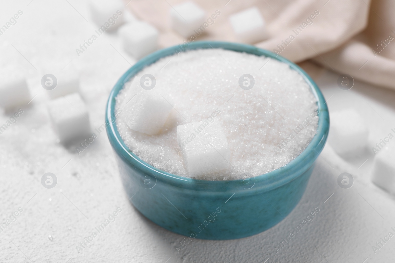 Photo of Different types of sugar in bowl on white table, closeup