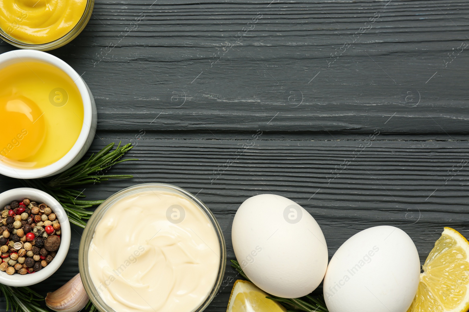 Photo of Glass bowl with fresh mayonnaise and ingredients on black wooden table, flat lay. Space for text