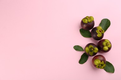 Photo of Fresh ripe mangosteen fruits with green leaves on pink background, flat lay. Space for text