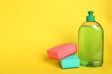 Photo of Detergent and sponges on yellow background, space for text