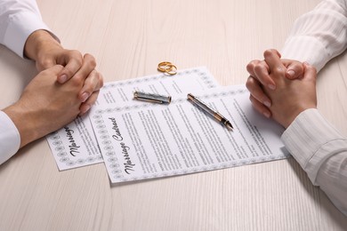 Man and woman signing marriage contract at light wooden table, closeup