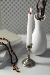Photo of Books, burning candle, rosary beads and vase of willow branches on white table, closeup
