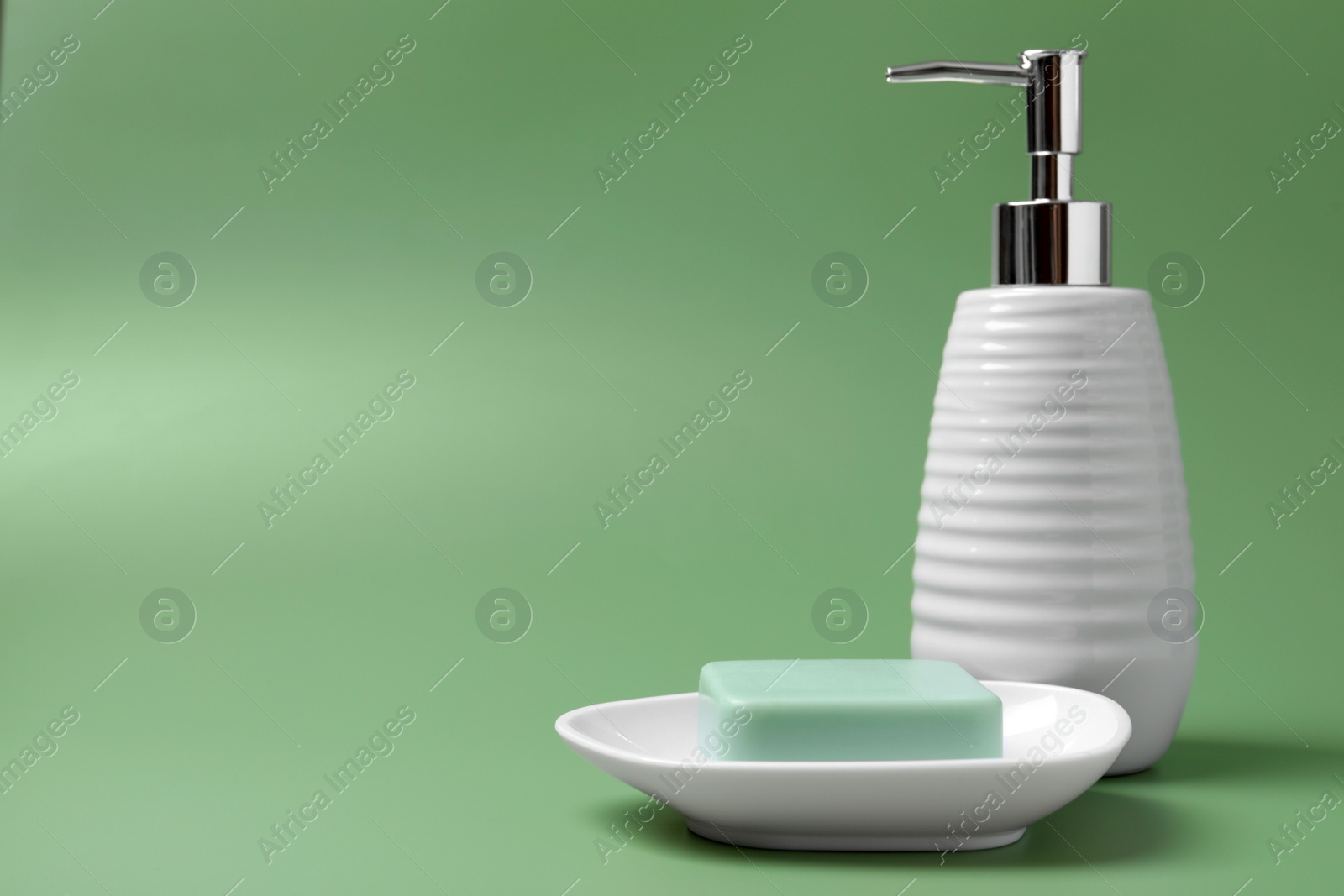 Photo of Soap bar and bottle dispenser on green background, space for text