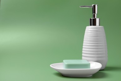 Soap bar and bottle dispenser on green background, space for text