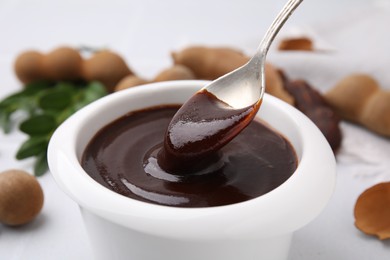 Photo of Taking tasty tamarind sauce with spoon from bowl on table, closeup