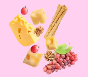 Cheese, breadsticks, grapes and walnut falling against light pink background