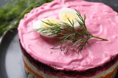 Photo of Herring under fur coat salad on black plate, closeup. Traditional Russian dish