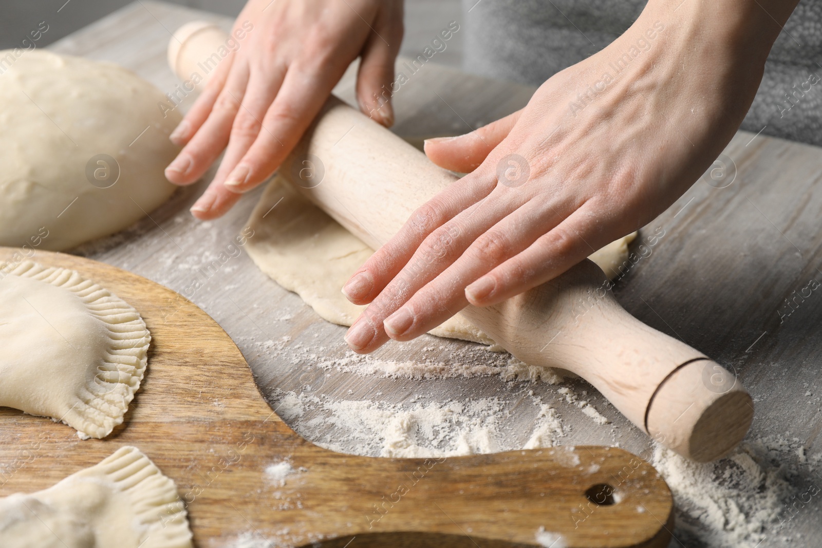 Photo of Woman rolling dough for chebureki at wooden table, closeup