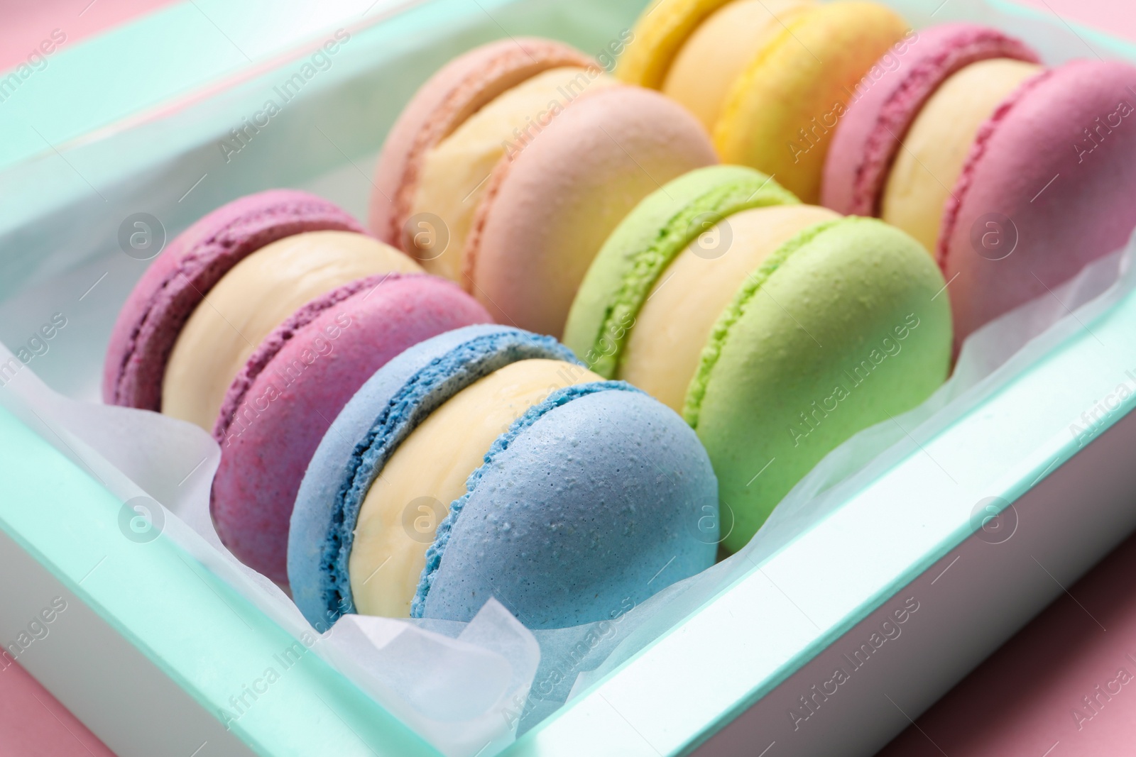 Photo of Many delicious colorful macarons in box on pink background, closeup
