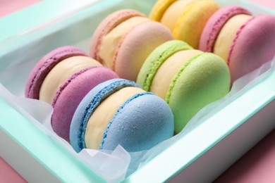 Many delicious colorful macarons in box on pink background, closeup