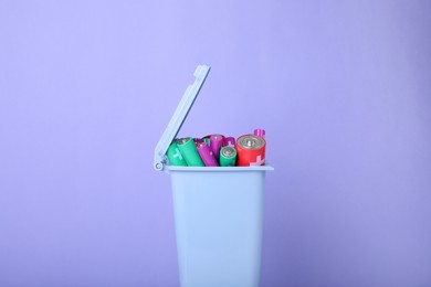 Photo of Many used batteries in recycling bin on light purple background