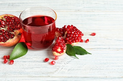 Photo of Glass of pomegranate juice and fresh fruits on wooden background, space for text