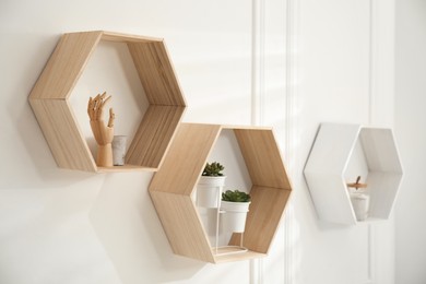 Photo of Honeycomb shaped shelves with decorative elements and houseplants on white wall