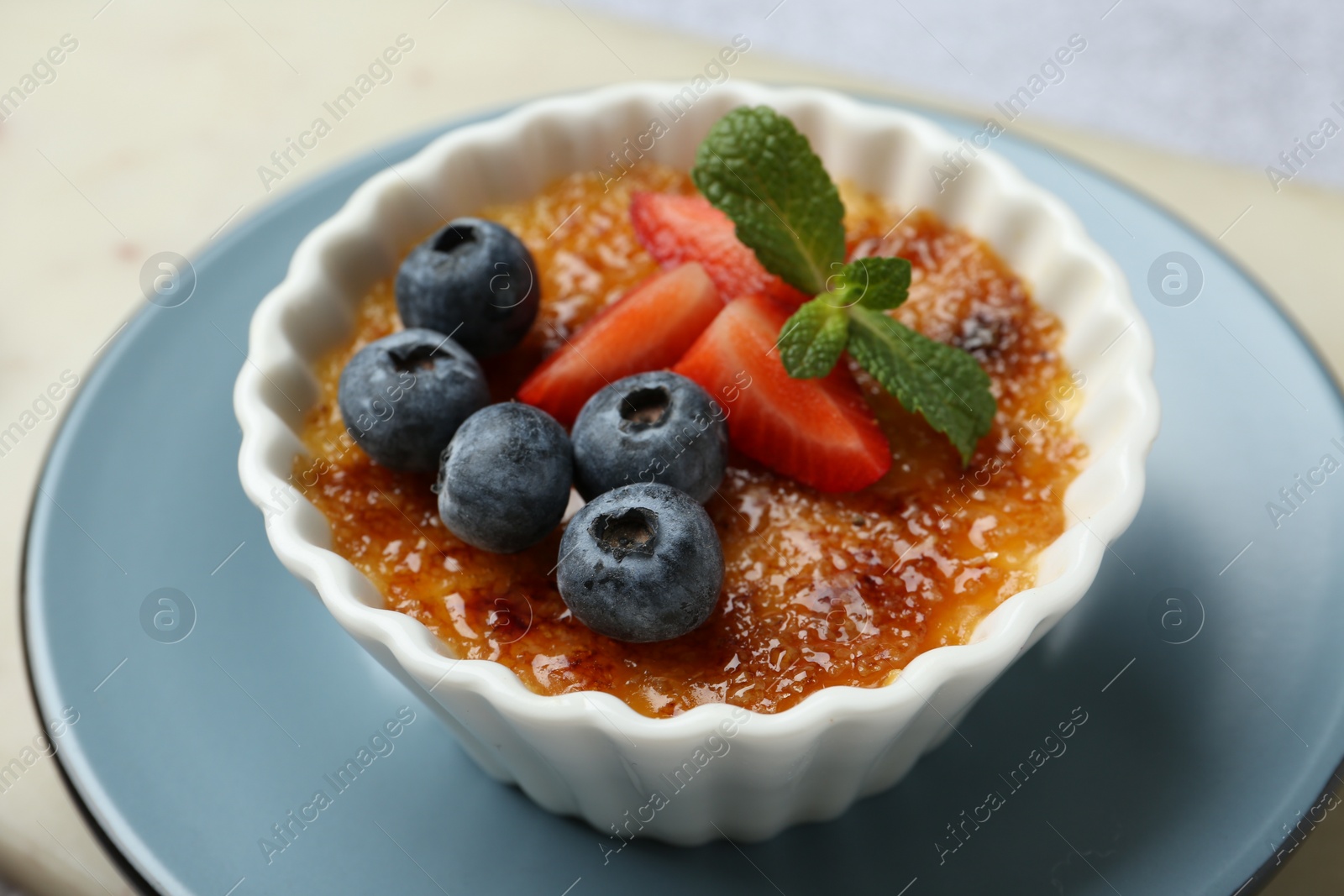 Photo of Delicious creme brulee with berries and mint in bowl on table, closeup