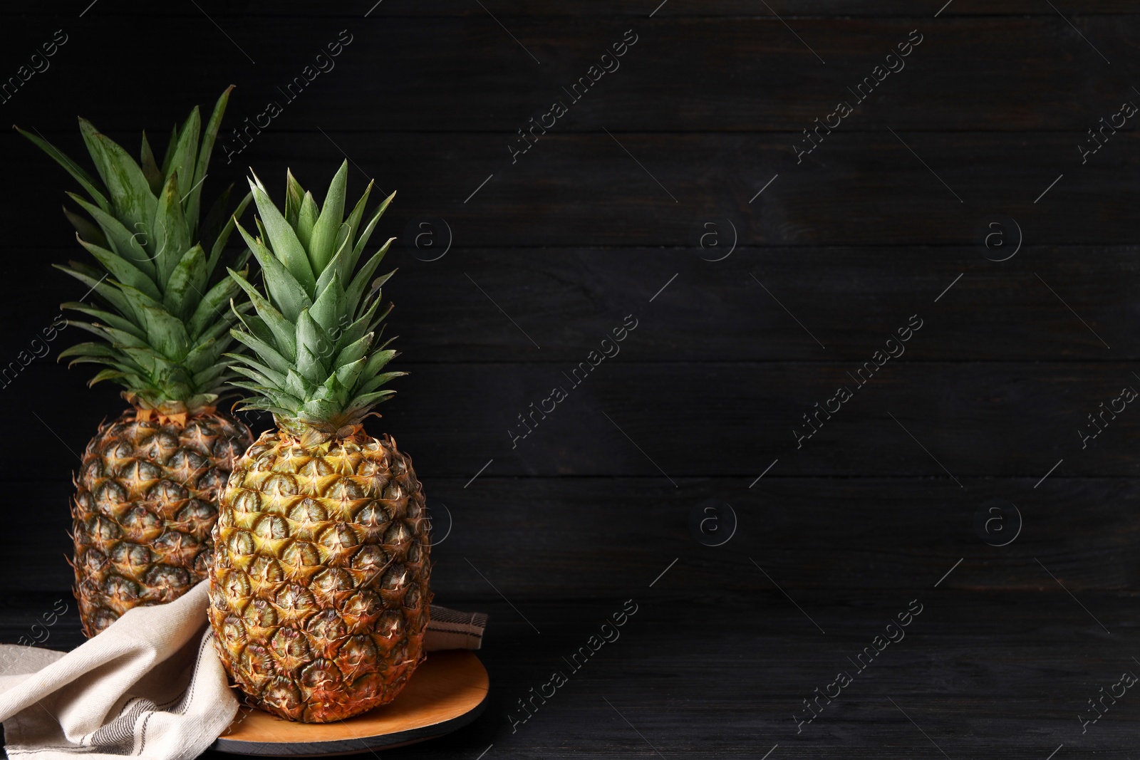 Photo of Whole ripe pineapples on black table, space for text