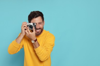 Man with camera taking photo on light blue background, space for text. Interesting hobby